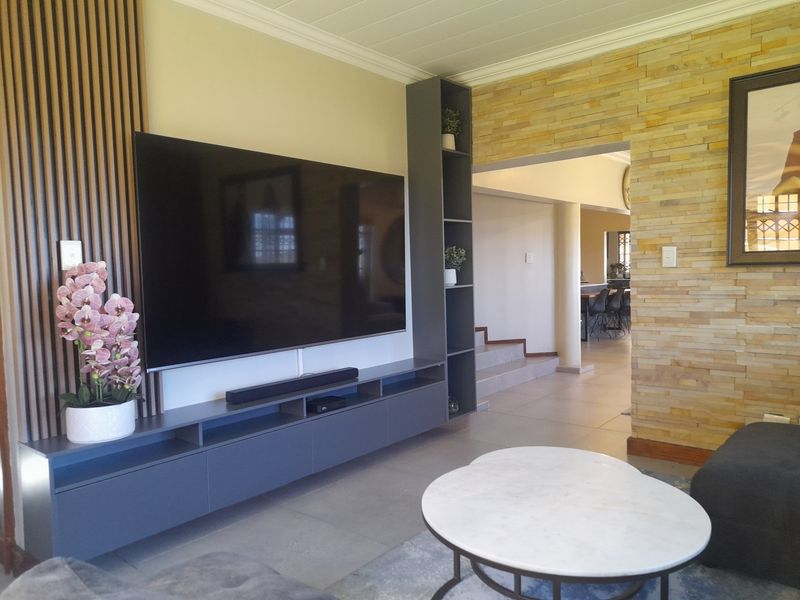 A modern living room featuring a custom built-in media unit, striking stone-clad feature wall, and elegant timber slat paneling with neutral tiled flooring.