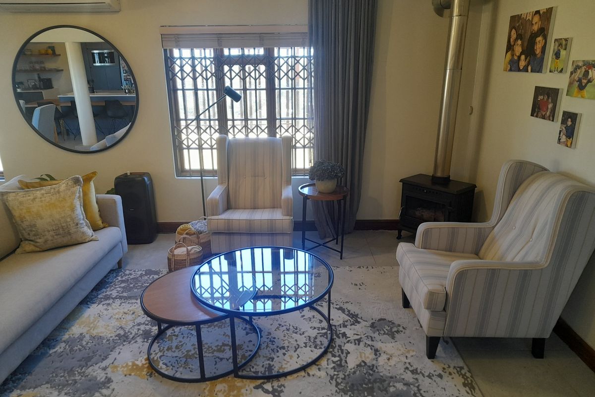 A comfortable living room featuring a freestanding fireplace, tiled flooring, and a large window with security gate, providing a cozy and functional space.