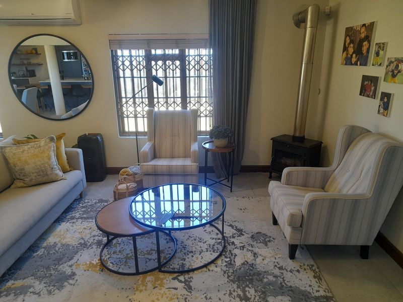 A comfortable living room featuring a freestanding fireplace, tiled flooring, and a large window with security gate, providing a cozy and functional space.
