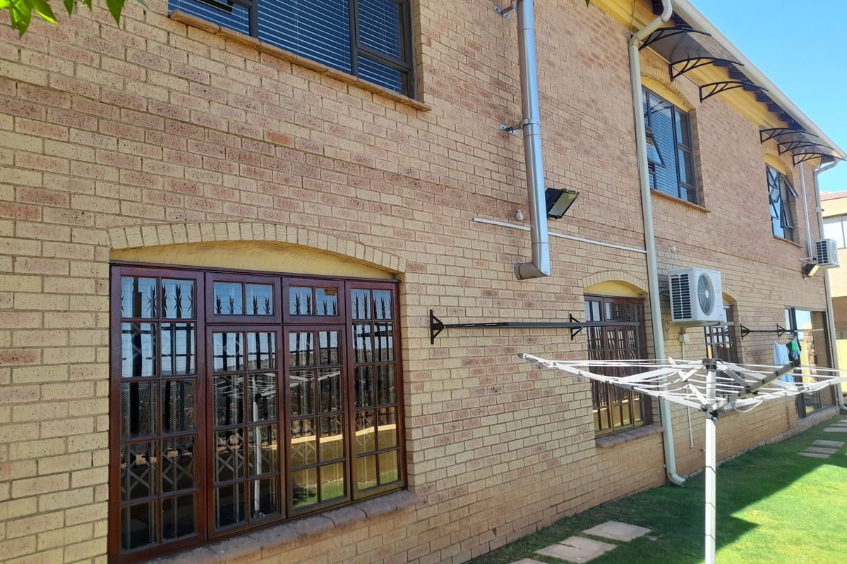 Rear exterior view of the face brick cluster home featuring timber window frames, security bars, and an external air conditioning unit.