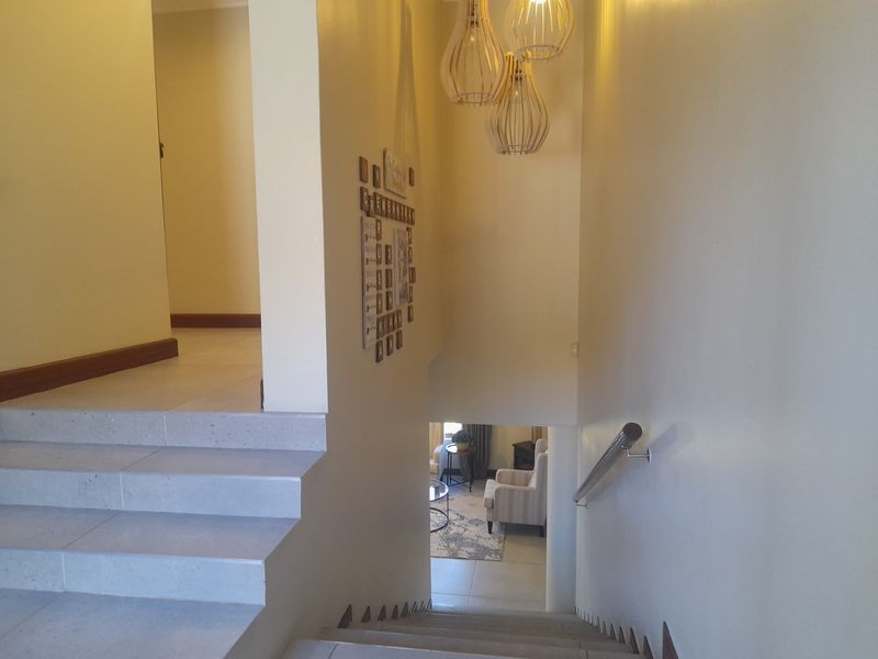 A bright hallway featuring a tiled staircase with a metal handrail, leading down to a lower living area with neutral wall finishes.