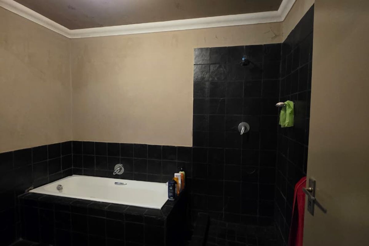 A bathroom featuring a built-in bathtub and a separate shower enclosure with dark tiled finishes and neutral wall paint.