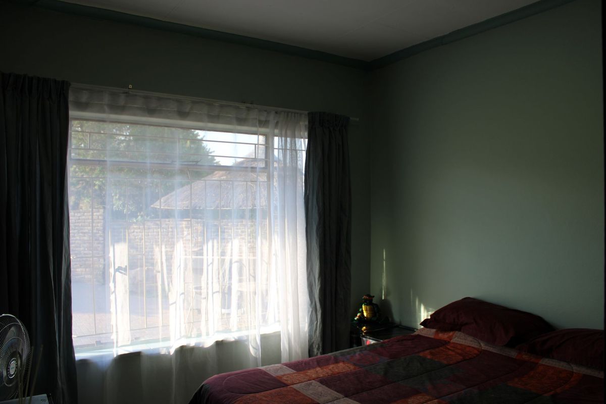 A bedroom featuring a large window with security bars, providing natural light and a view of the exterior area.