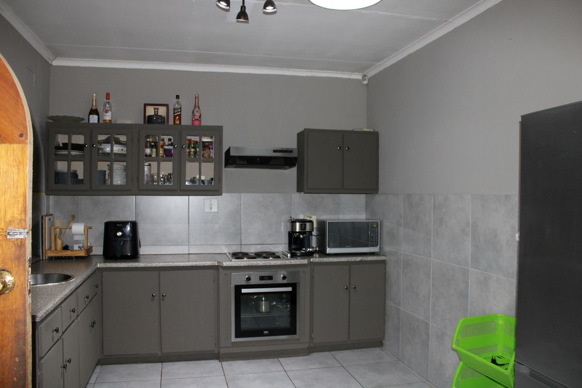 A functional kitchen featuring grey cabinetry, tiled splashbacks, built-in oven and hob, and tiled flooring.
