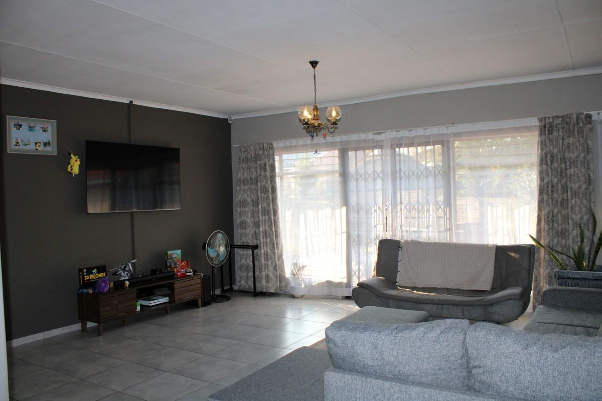 A spacious living room featuring tiled flooring, a dark accent wall, and large sliding glass doors that provide access to the exterior.