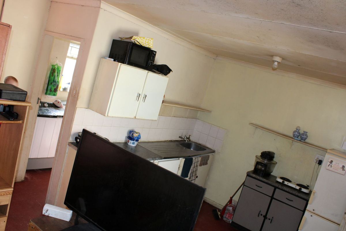A dated kitchen area featuring basic cabinetry, a stainless steel sink, and tiled splashbacks, requiring cosmetic updates and maintenance to improve functionality and aesthetic appeal.