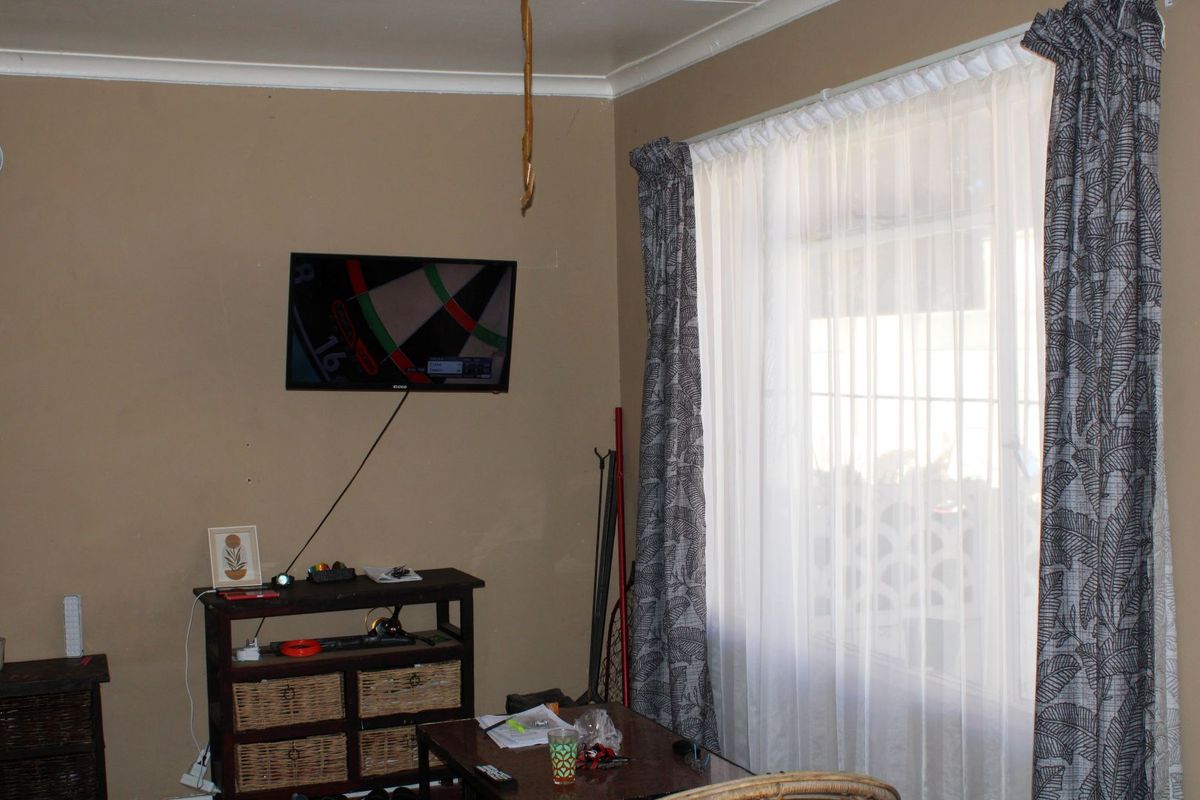 A living room area featuring a window with curtains and wall-mounted television, showing signs of wear including wall cracks.