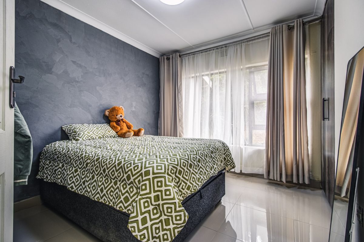 A well-maintained bedroom featuring a textured feature wall, tiled flooring, and large windows with curtain tracks.