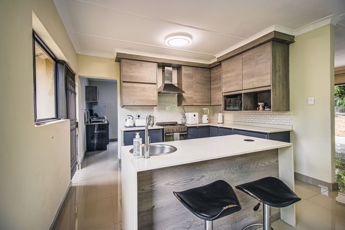 Modern kitchen featuring wood-grain cabinetry, a central island with a prep sink, subway tile backsplash, and integrated stainless steel appliances.