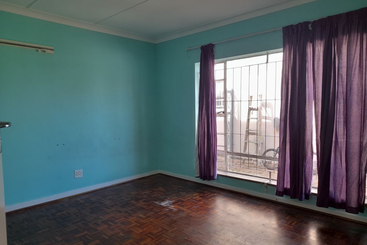 A vacant bedroom featuring original parquet flooring, large window with security bars, and teal-painted walls.