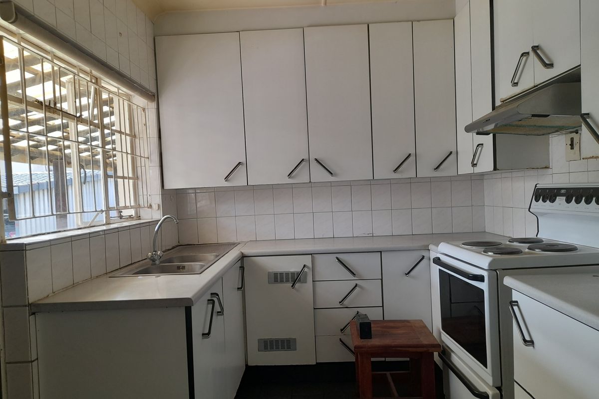 A dated kitchen featuring white cabinetry, a stainless steel sink, and a freestanding electric stove with an extractor fan.