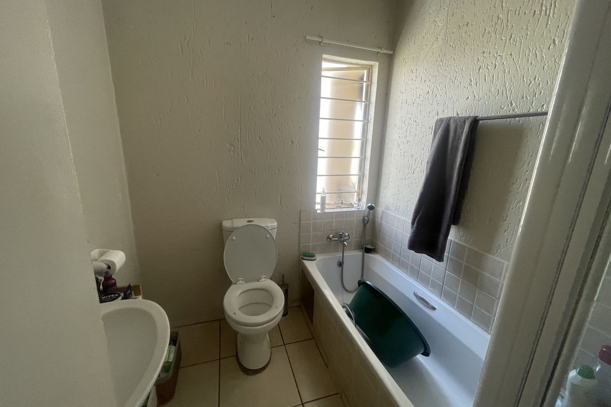 A compact bathroom featuring a standard bathtub with shower mixer, a toilet, and a pedestal basin, finished with textured walls and tiled flooring.