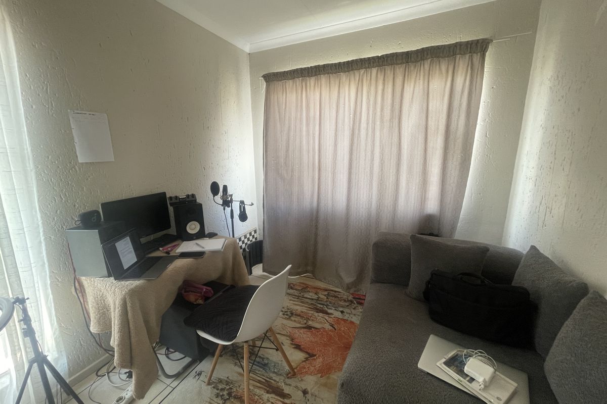 A functional bedroom or home office space featuring tiled flooring and a window with curtain treatments.