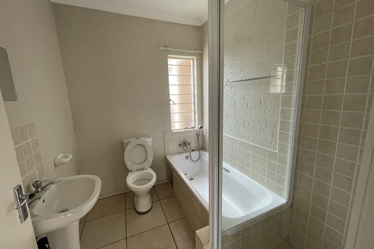 A functional bathroom featuring a pedestal basin, a toilet, and a combined bathtub with a shower screen.
