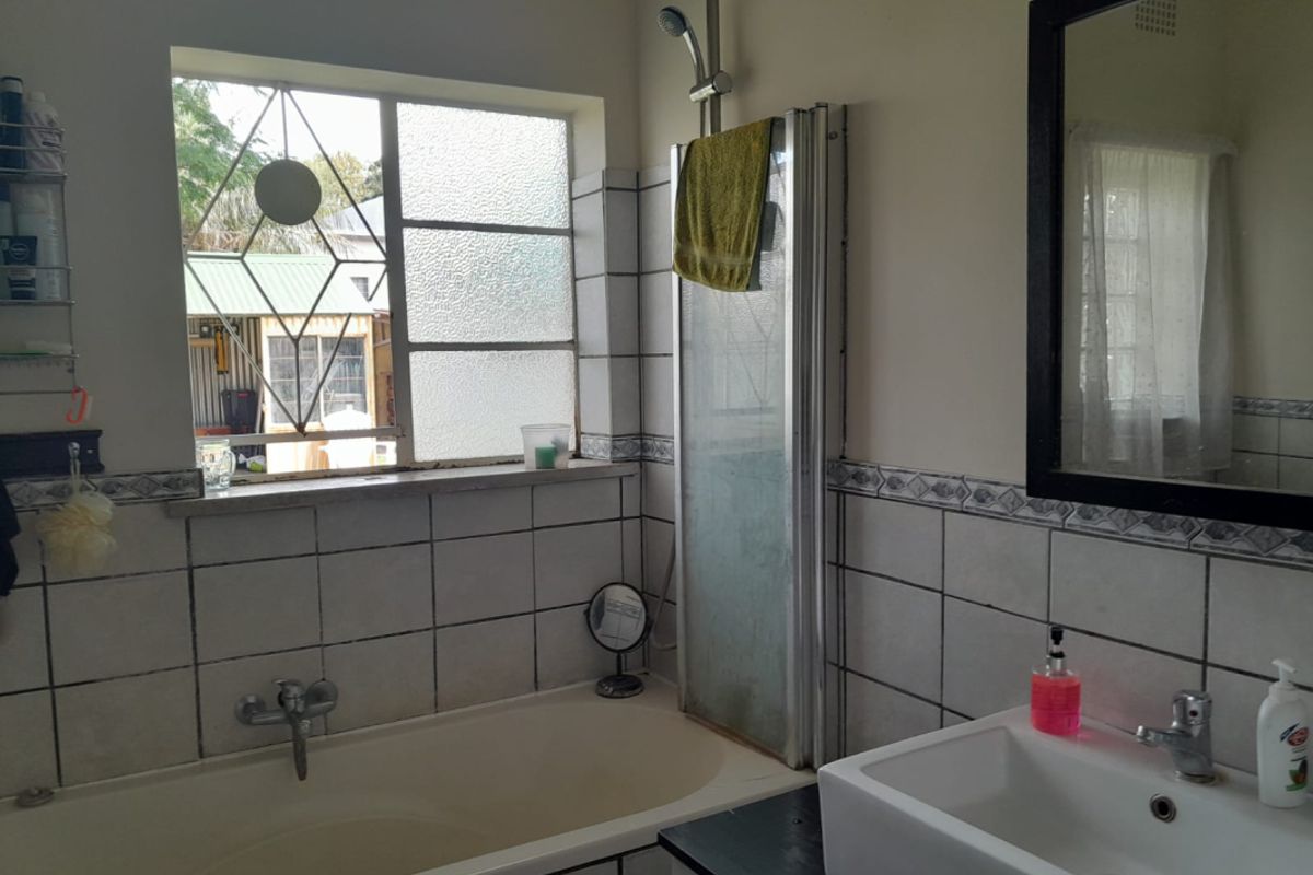 A functional bathroom featuring a built-in bathtub with shower attachment, a modern vessel sink, and a window with security bars.
