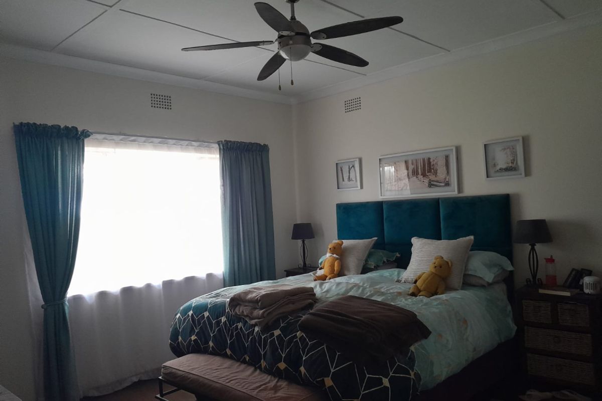 A well-lit bedroom featuring a ceiling fan, large window with curtains, and neutral wall finishes.