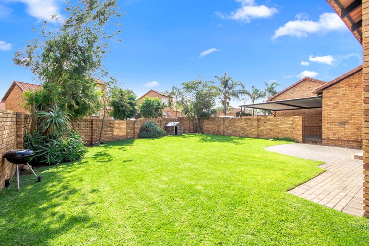 A spacious private rear garden featuring a well-maintained lawn, perimeter brick boundary walls, and a paved patio area.