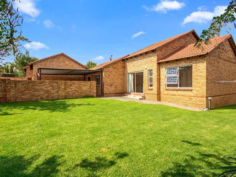 A spacious private rear garden featuring a well-maintained lawn, face-brick exterior walls, and a covered patio area.