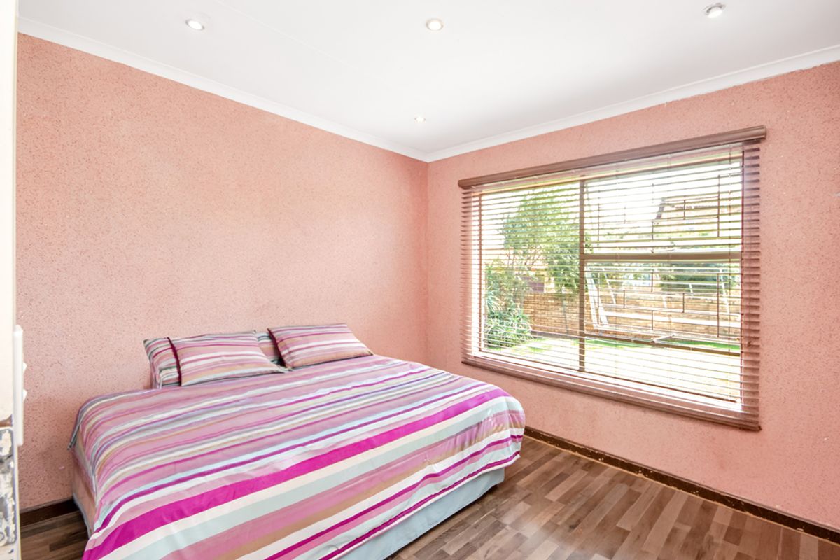 A bedroom featuring wood-look flooring, recessed ceiling lighting, and a large window with fitted blinds overlooking the garden.