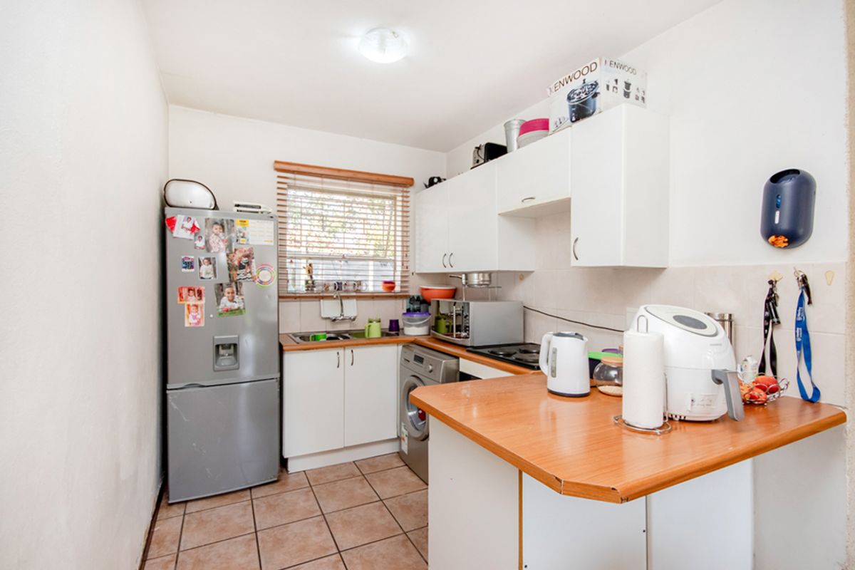 Compact kitchen featuring white cabinetry, wood-look laminate countertops, tiled flooring, and a window with fitted blinds.