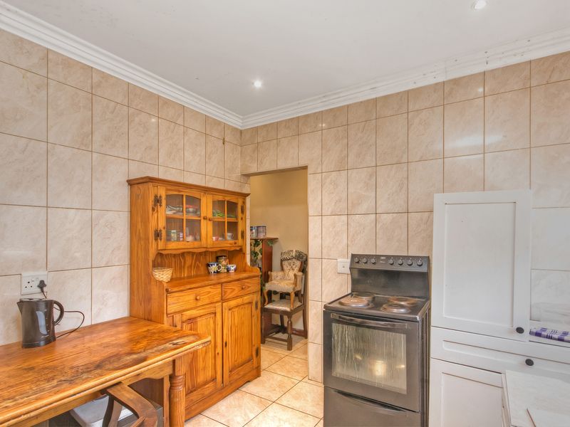 A functional kitchen featuring tiled walls and flooring, equipped with a freestanding stove and built-in cabinetry, with an adjacent scullery area.