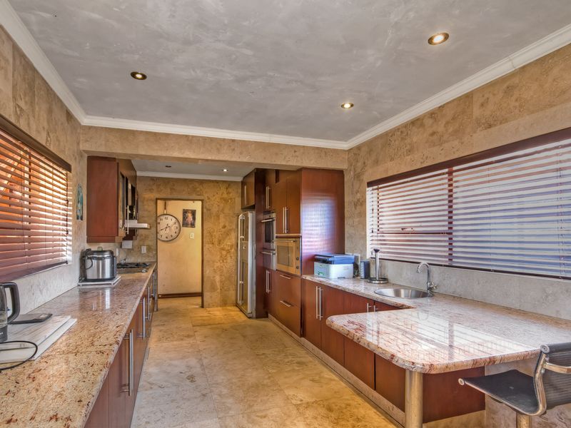 Spacious kitchen featuring granite countertops, extensive built-in cabinetry, integrated appliances, stone wall and floor finishes, and ample natural light through venetian blinds.