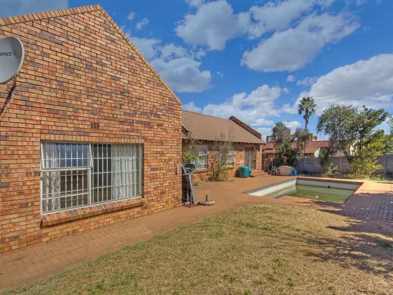 Rear view of a brick house featuring a paved patio area and an in-ground swimming pool in need of maintenance.