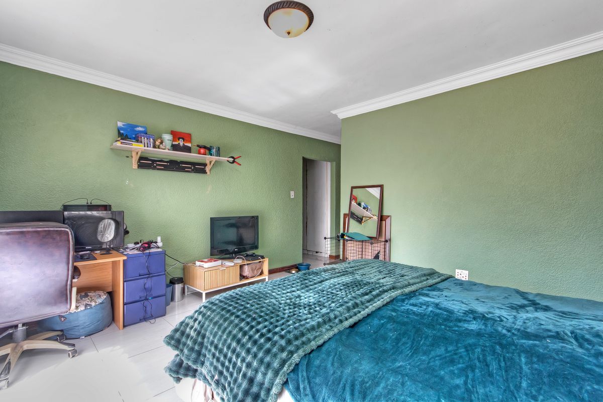 A bedroom featuring tiled flooring, ceiling cornice, and green textured walls, providing a functional space with standard electrical fixtures.