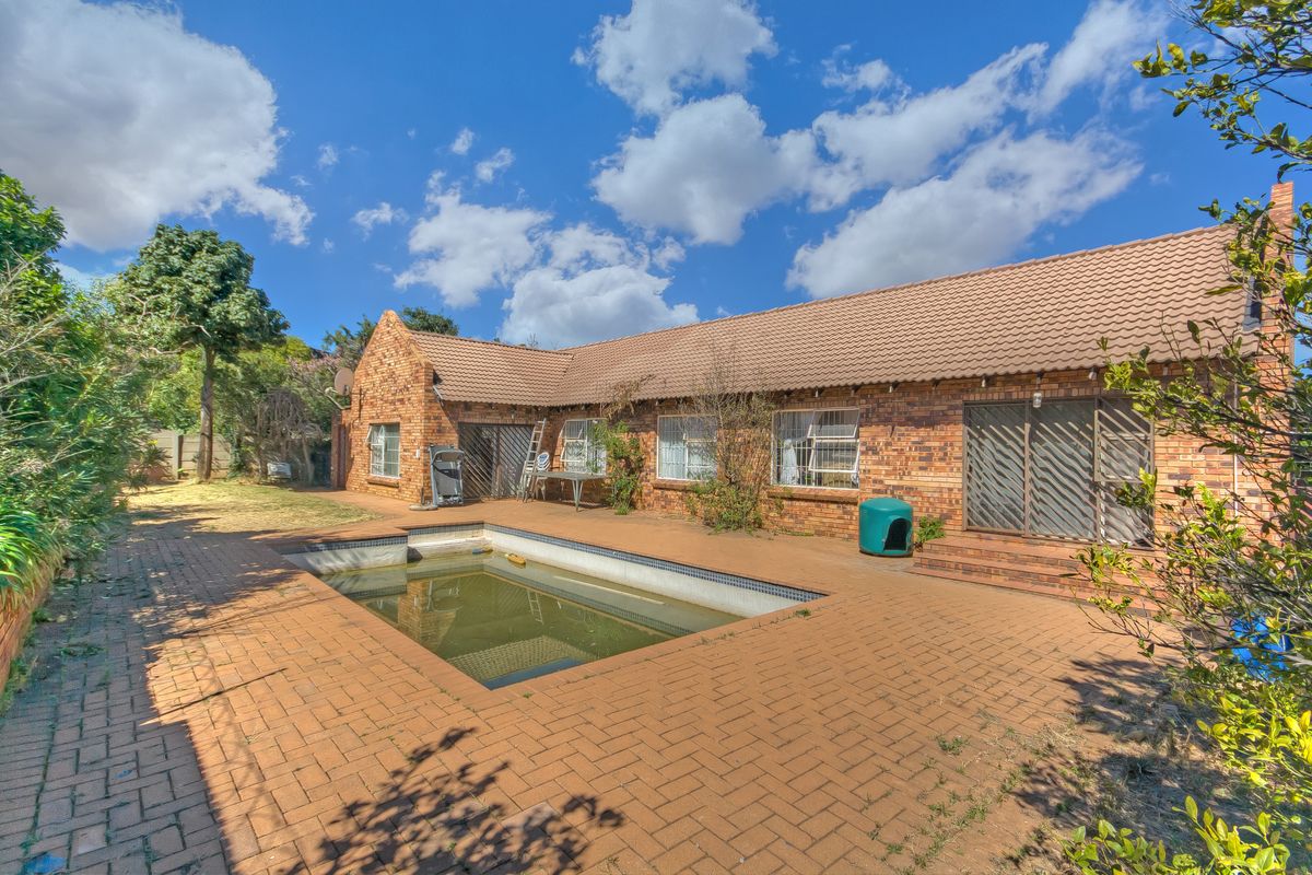 Rear exterior view of a facebrick house featuring a swimming pool and paved patio area, requiring maintenance and landscaping.