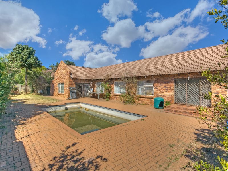 Rear exterior view of a facebrick house featuring a swimming pool and paved patio area, requiring maintenance and landscaping.