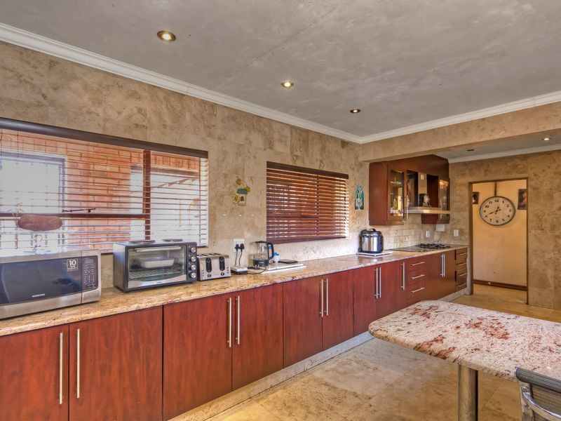 Spacious kitchen featuring extensive wooden cabinetry, granite countertops, stone wall and floor tiling, and integrated cooking appliances.