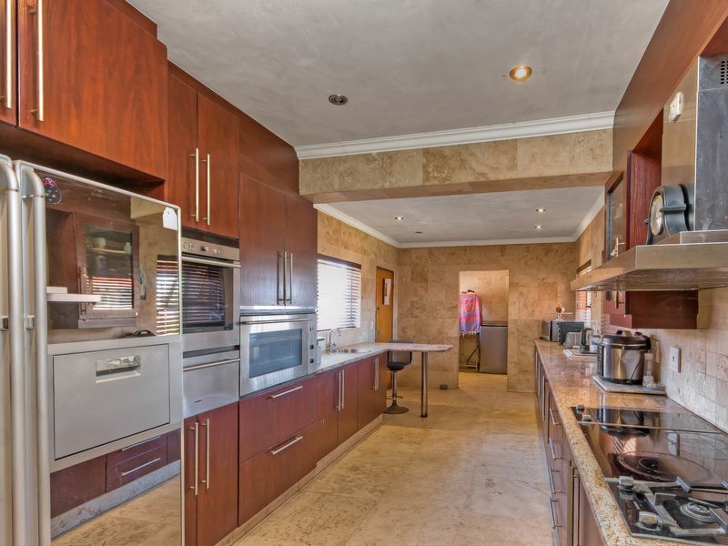 Spacious kitchen featuring extensive built-in cabinetry, stone wall cladding, stone tile flooring, and integrated appliances including an oven, microwave, and hob.
