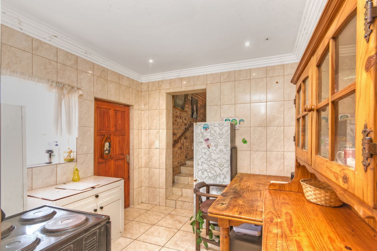 A dated kitchen featuring full-height wall tiling, tiled floors, and built-in cabinetry, with visible signs of ceiling wear and water damage.