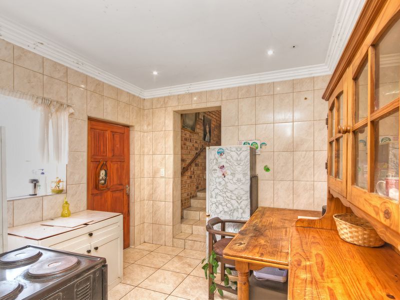 A dated kitchen featuring full-height wall tiling, tiled floors, and built-in cabinetry, with visible signs of ceiling wear and water damage.