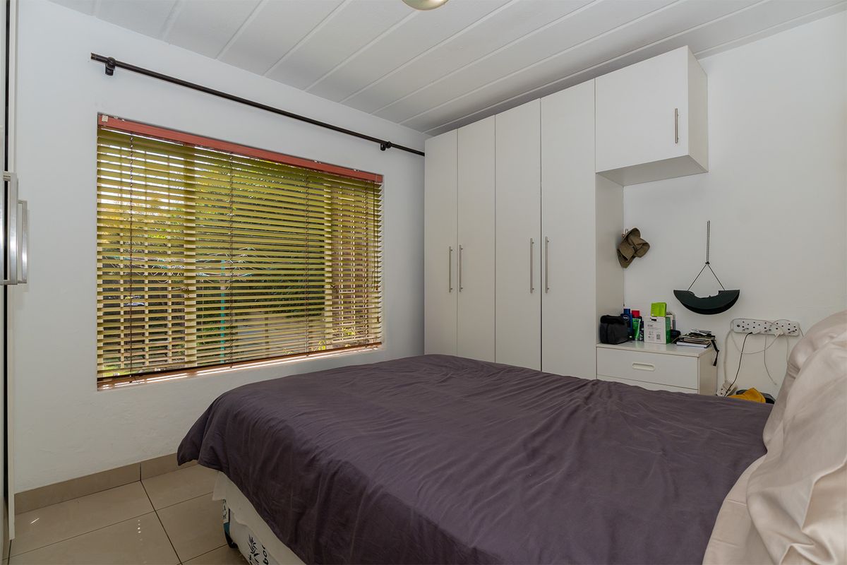 A bedroom featuring built-in white cabinetry, tiled flooring, and a window fitted with horizontal blinds.