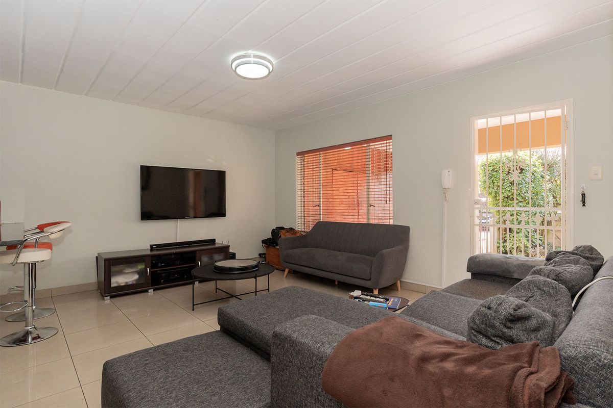A spacious living area featuring tiled flooring, a ceiling-mounted light fixture, and a security gate leading to the exterior.