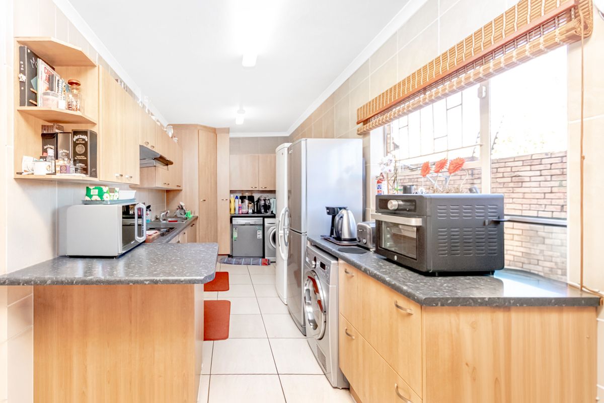 A functional kitchen featuring light wood cabinetry, laminate countertops, tiled flooring, and integrated space for laundry appliances.