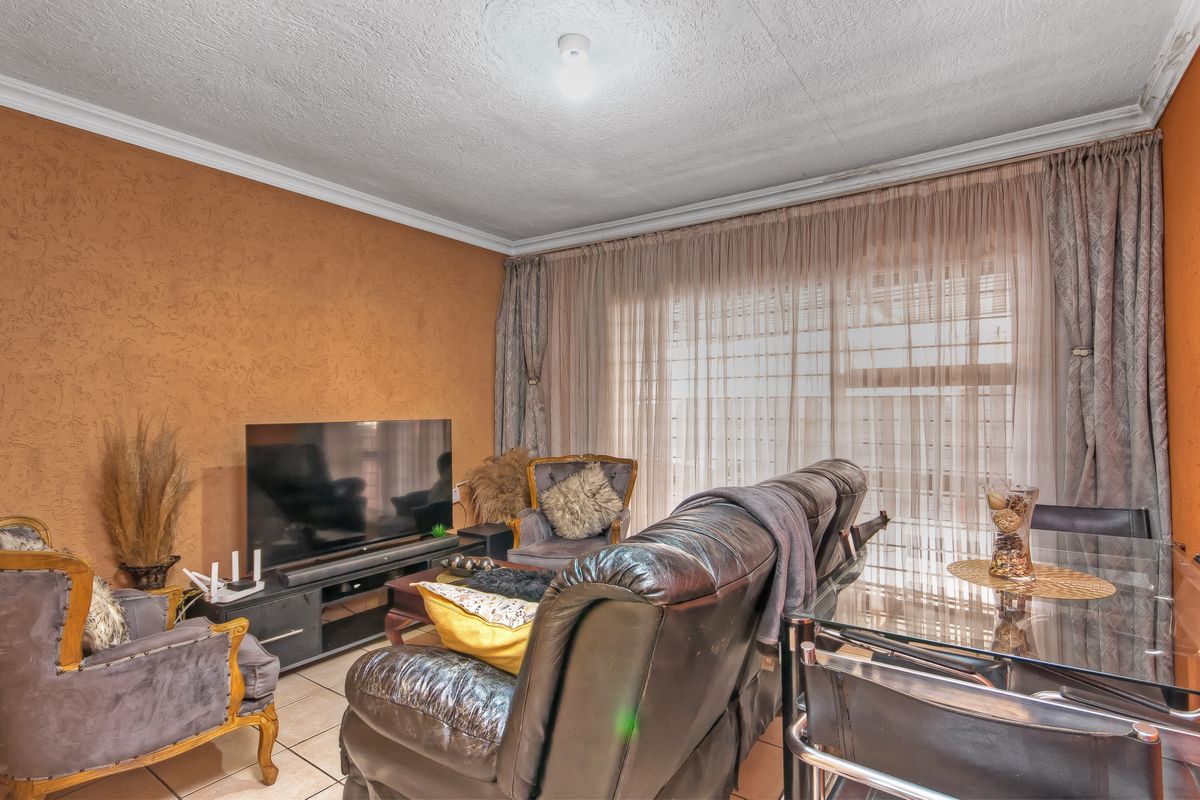 A living room featuring textured walls, tiled flooring, and large windows with curtains, providing a functional and lived-in space.