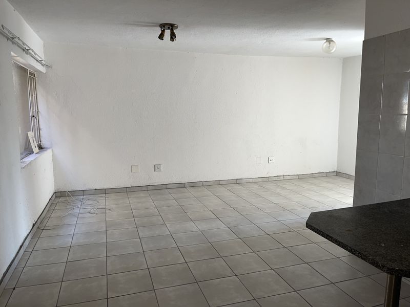 An empty open-plan living and kitchen area featuring neutral tiled flooring, a breakfast bar, and basic lighting fixtures, ready for personalization.