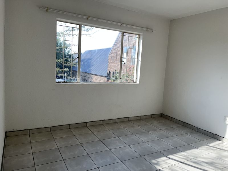 An empty bedroom featuring tiled flooring, a window with security bars, and a curtain rail, ready for personalization.
