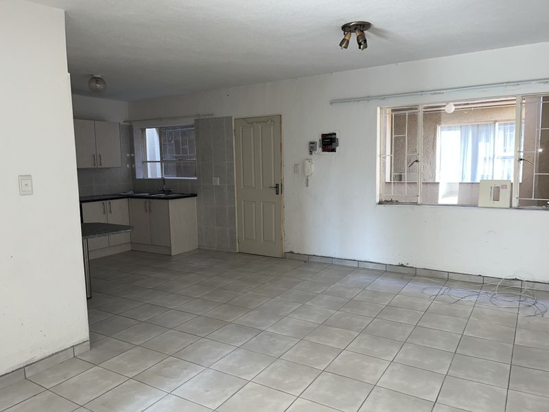 Open plan living and kitchen area featuring tiled flooring, built-in cabinetry, and security bars on windows. The space is vacant and requires cosmetic updates.