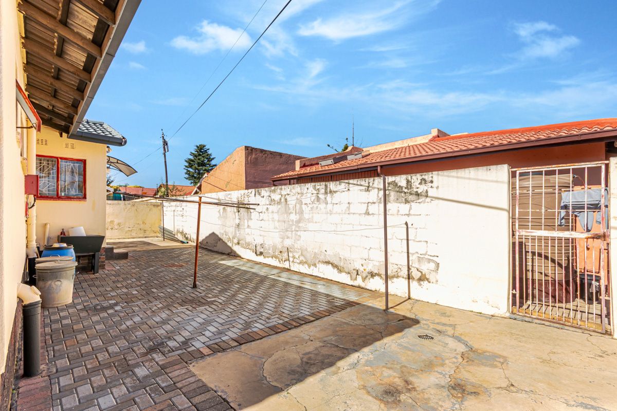 A paved rear courtyard area featuring a perimeter boundary wall, metal security gate, and a fixed washing line structure.