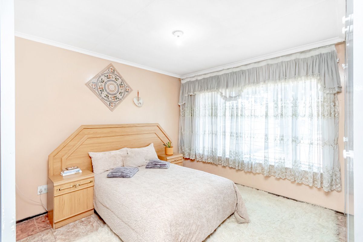 A bedroom featuring a built-in wooden headboard with integrated bedside tables and a large window with curtain pelmet.