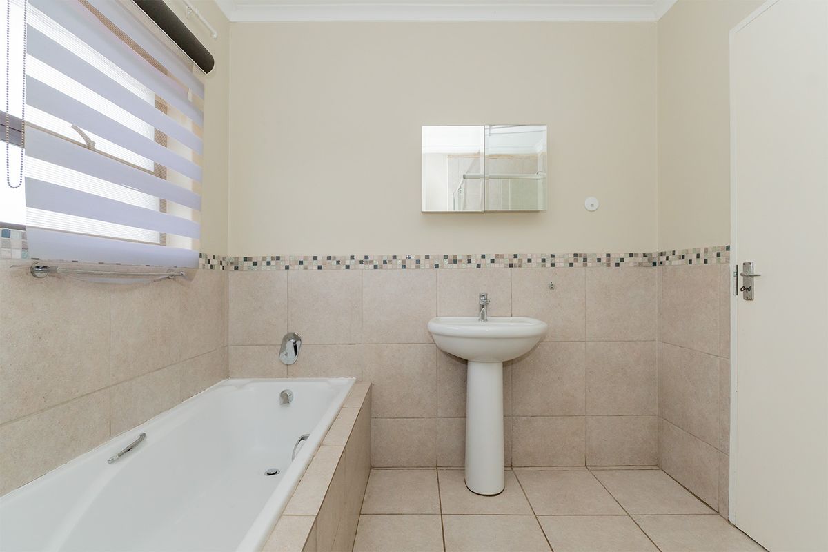 A functional bathroom featuring a built-in bathtub, pedestal basin, and neutral tiled walls with a decorative mosaic border.