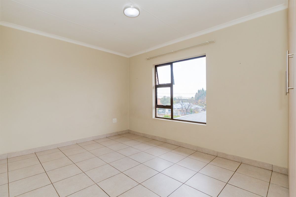 A bright, empty bedroom featuring neutral tiled flooring, a large window with natural light, and built-in cupboard space.
