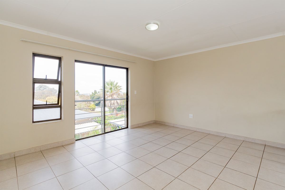 A bright, empty living area featuring neutral tiled flooring, large sliding glass doors leading to a balcony, and a separate window for natural light.