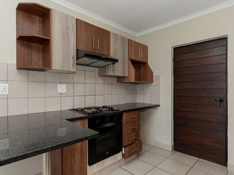 Compact kitchen featuring two-tone cabinetry, granite countertops, built-in oven, hob, and extractor fan with tiled flooring and backsplash.