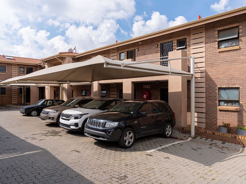 Exterior view of the apartment complex featuring paved parking bays with shade cloth carports and face-brick facade.