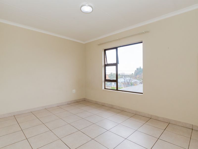 A bright, empty bedroom featuring neutral tiled flooring, a large window with natural light, and built-in cupboard space.