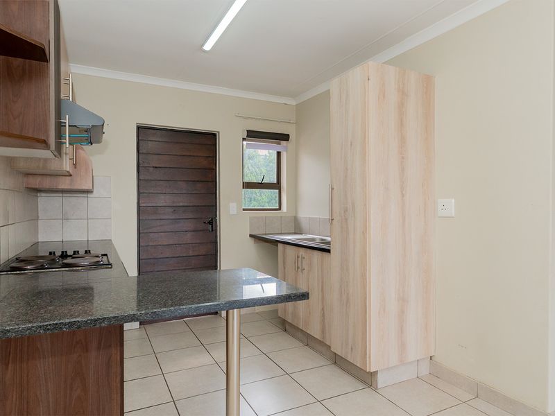 A functional kitchen featuring granite countertops, built-in cabinetry, a gas hob, and tiled flooring with direct access to an exterior door.